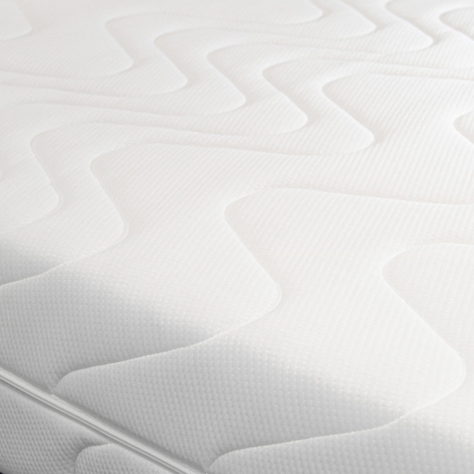 Nahaufnahme einer weißen Wende-Kaltschaummatratze mit wellenförmigem Muster auf der Oberfläche, seitliche Perspektive.