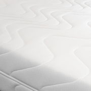 Nahaufnahme einer weißen Wende-Kaltschaummatratze mit wellenförmigem Muster auf der Oberfläche, seitliche Perspektive.