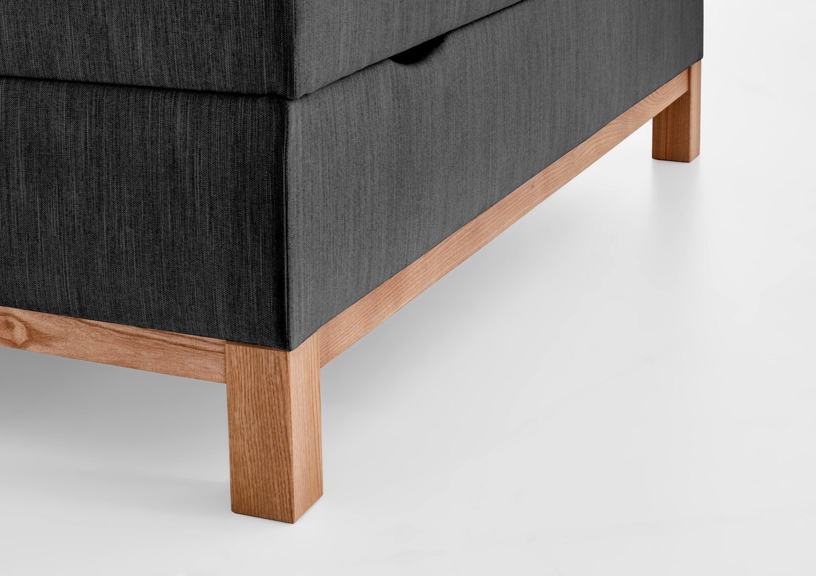 Nahaufnahme eines Boxspringbettes mit grauem Stoffbezug und Holzfüßen, seitliche Perspektive