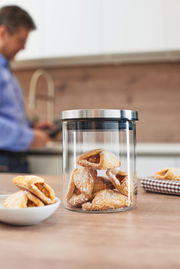 Glasdose Comodo 500ml mit Gebäck gefüllt, auf einem Holztisch in einer Küche platziert, im Hintergrund eine Person unscharf zu sehen.