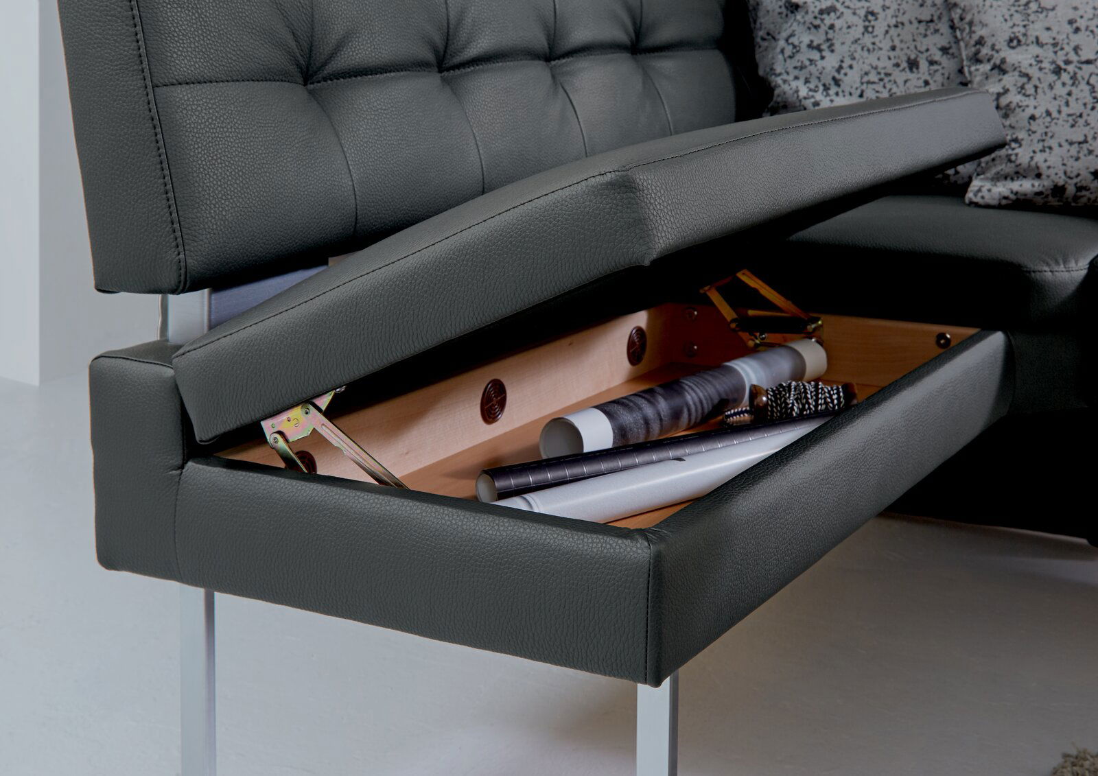 Dieter Knoll Eckbank LIMONE Nahaufnahme einer Eckbank mit aufklappbarem Stauraum unter der Sitzfläche, in dem verschiedene Gegenstände aufbewahrt werden. Perspektive von der Seite.