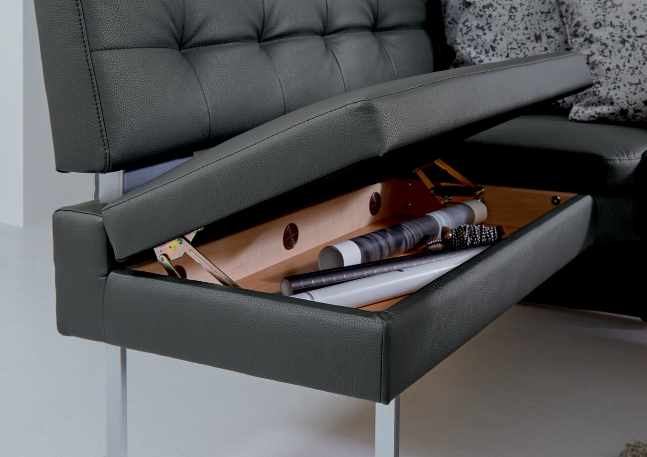 Dieter Knoll Eckbank LIMONE Nahaufnahme einer Eckbank mit aufklappbarem Stauraum unter der Sitzfläche, in dem verschiedene Gegenstände aufbewahrt werden. Perspektive von der Seite.