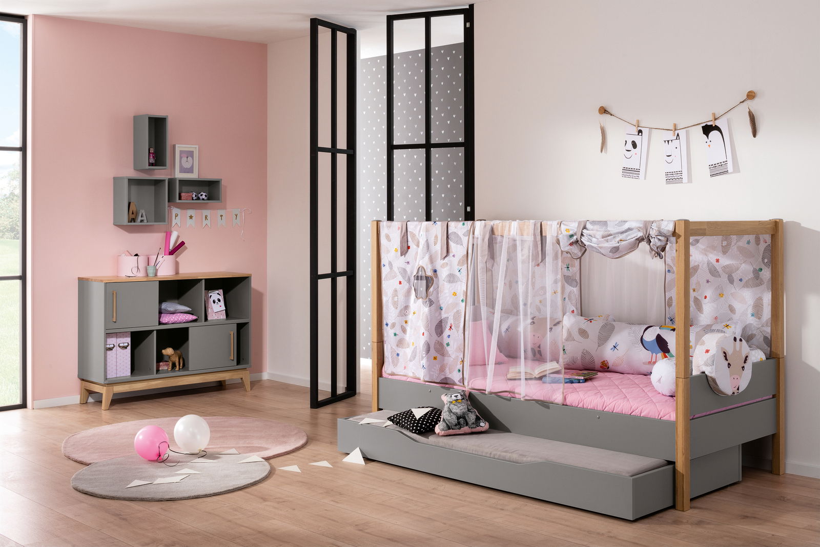 Kinderzimmer mit einem grauen Highboard und einem Spielbett mit Baldachin, dekoriert mit bunten Kissen und Vorhängen, aus der Perspektive von vorne rechts.