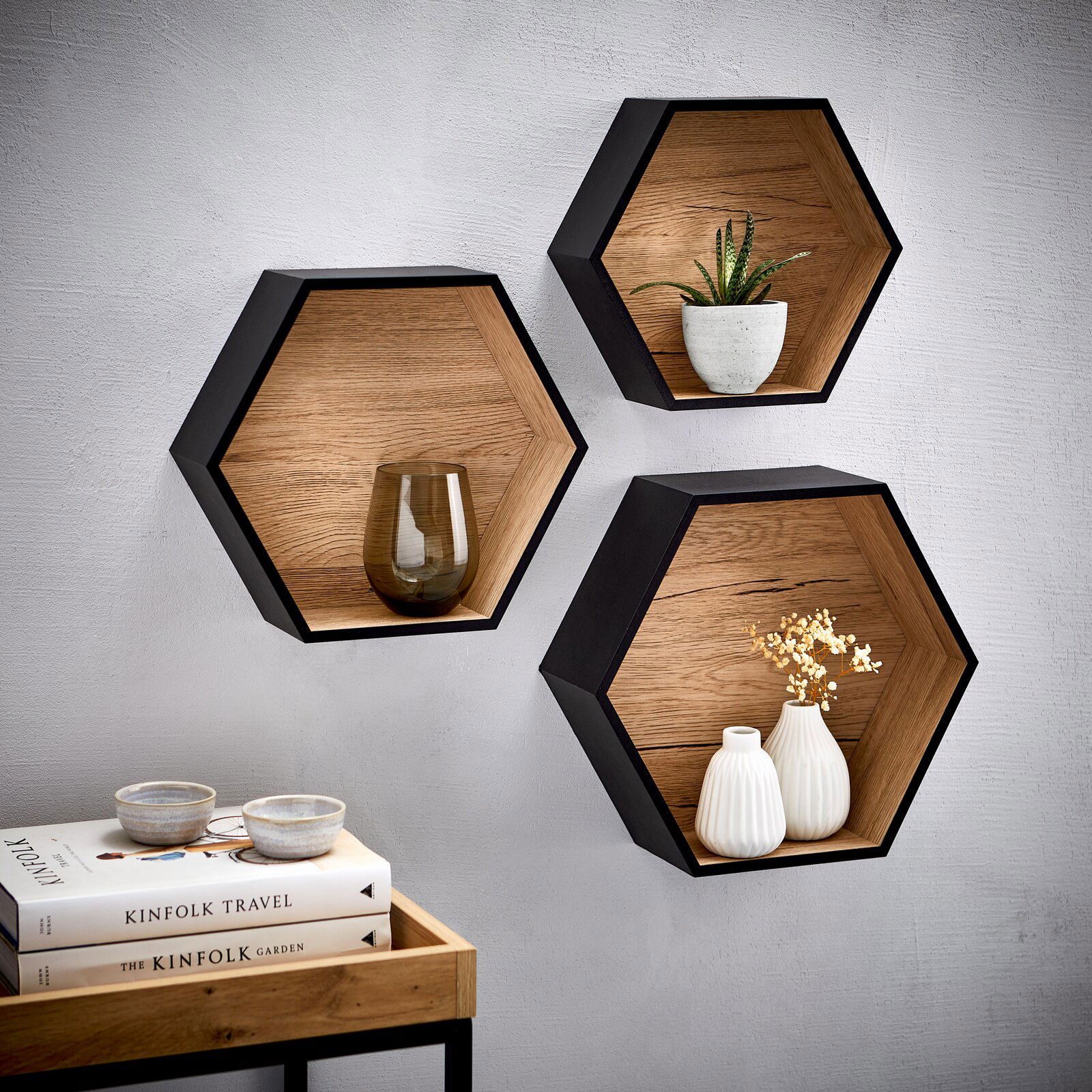 Dreiteiliges Wandregal-Set in Wabenform aus Holz mit schwarzem Rahmen, dekoriert mit Pflanzen und Vasen, seitliche Perspektive.