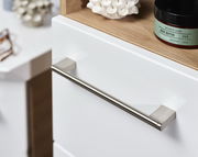 Nahaufnahme eines weißen Hochschranks mit Metallgriff und Holzablage, seitliche Perspektive.