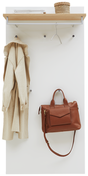 Garderobenpaneel mit Holzablage, Kleiderhaken und Hängemöglichkeiten, frontal fotografiert. Ein Mantel und eine braune Tasche sind aufgehängt, oben steht ein Korb.