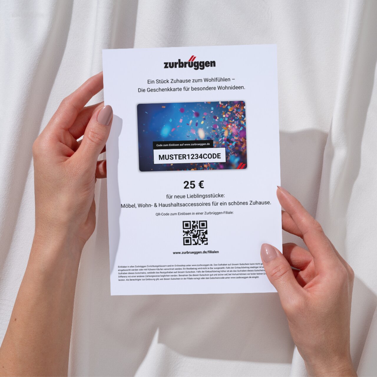 Zurbrüggen Digitaler Geschenkgutschein zum Ausdrucken Zwei Hände halten eine Zurbrüggen-Geschenkkarte im Wert von 25 Euro, mit einem QR-Code und der Aufschrift 'MUSTER1234CODE'.