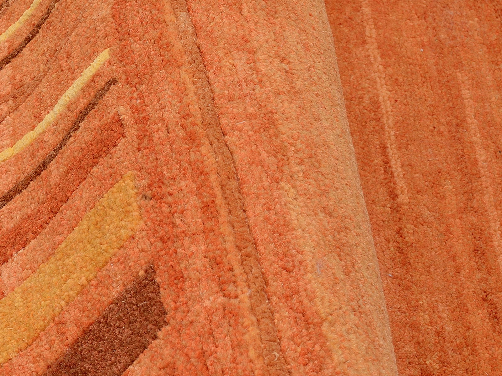 Nahaufnahme eines orangefarbenen Wollteppichs mit wellenförmigem Muster, von der Seite betrachtet.