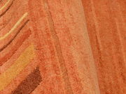 Nahaufnahme eines orangefarbenen Wollteppichs mit wellenförmigem Muster, von der Seite betrachtet.