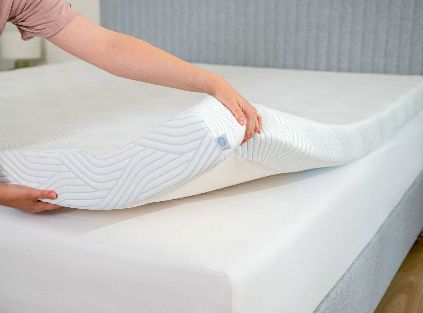 Nahaufnahme eines Toppers, der auf eine Matratze gelegt wird, mit einer Hand, die den Topper anhebt, um die Struktur und das Design zu zeigen.