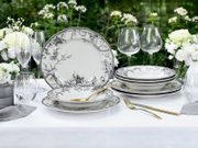Elegantes weißes Porzellan-Geschirrset mit schwarzem floralen Dekor (Teller und Schalen) auf gedecktem Tisch im Garten, frontal aus leichter Schrägansicht fotografiert.