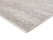 Nahaufnahme eines Designer Teppichs VELA ANTIQUE in Beige- und Grautönen mit antikem Muster, perspektivisch von der Seite aufgenommen.