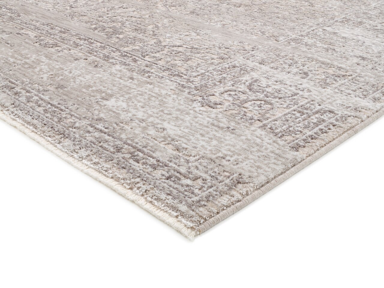 Nahaufnahme eines Designer Teppichs VELA ANTIQUE in Beige- und Grautönen mit antikem Muster, perspektivisch von der Seite aufgenommen.