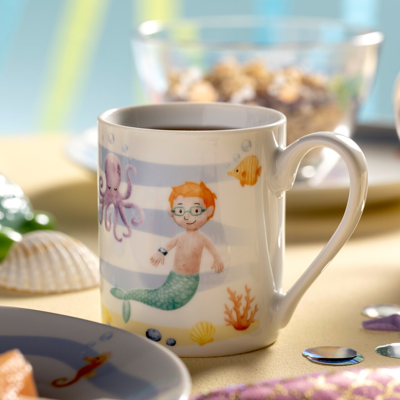 Tasse mit Meerjungfrauenmotiv, zeigt einen Jungen mit Brille als Meerjungmann, umgeben von einem Oktopus, Fischen und Korallen. Perspektive: seitlich.