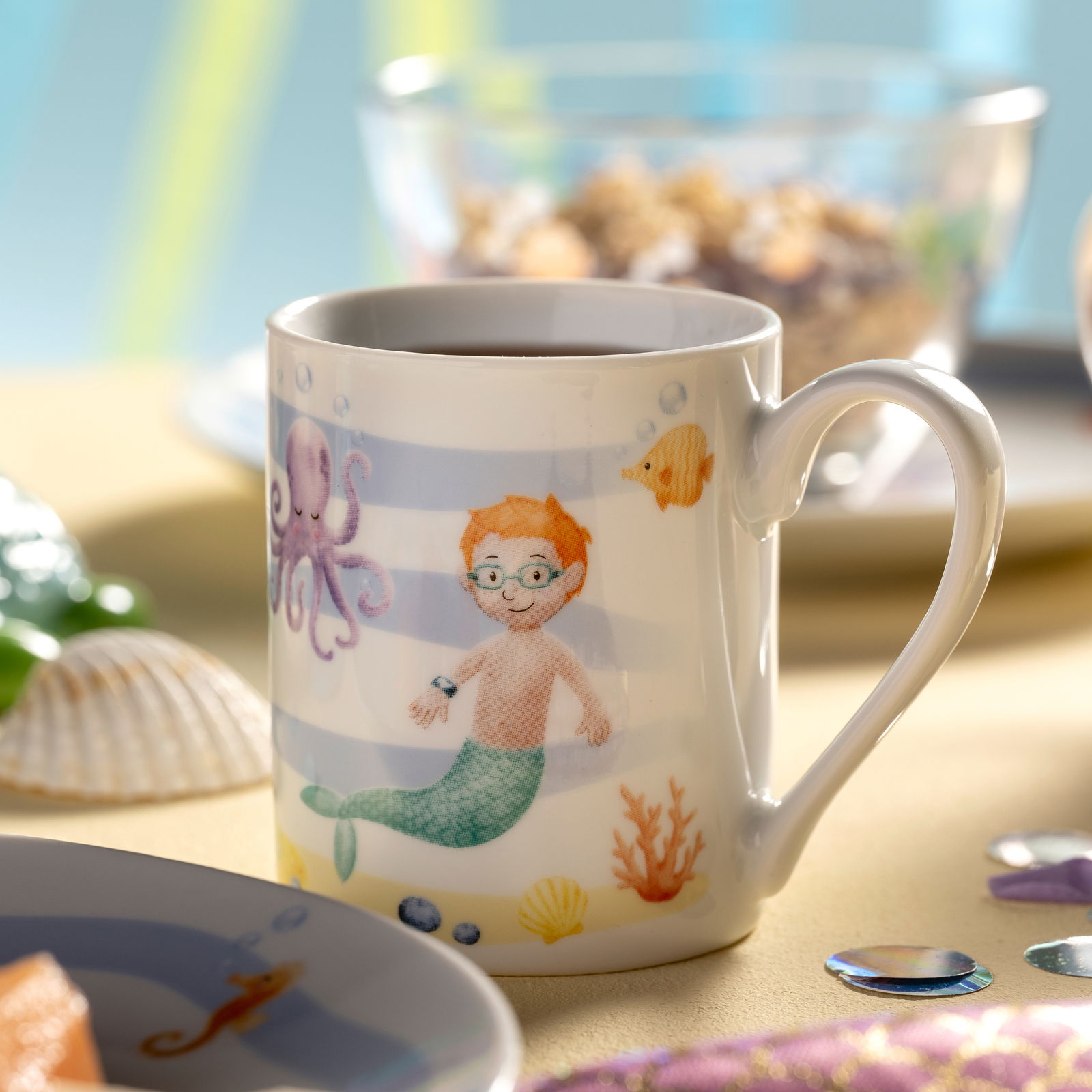Tasse mit Meerjungfrauenmotiv, zeigt einen Jungen mit Brille als Meerjungmann, umgeben von einem Oktopus, Fischen und Korallen. Perspektive: seitlich.