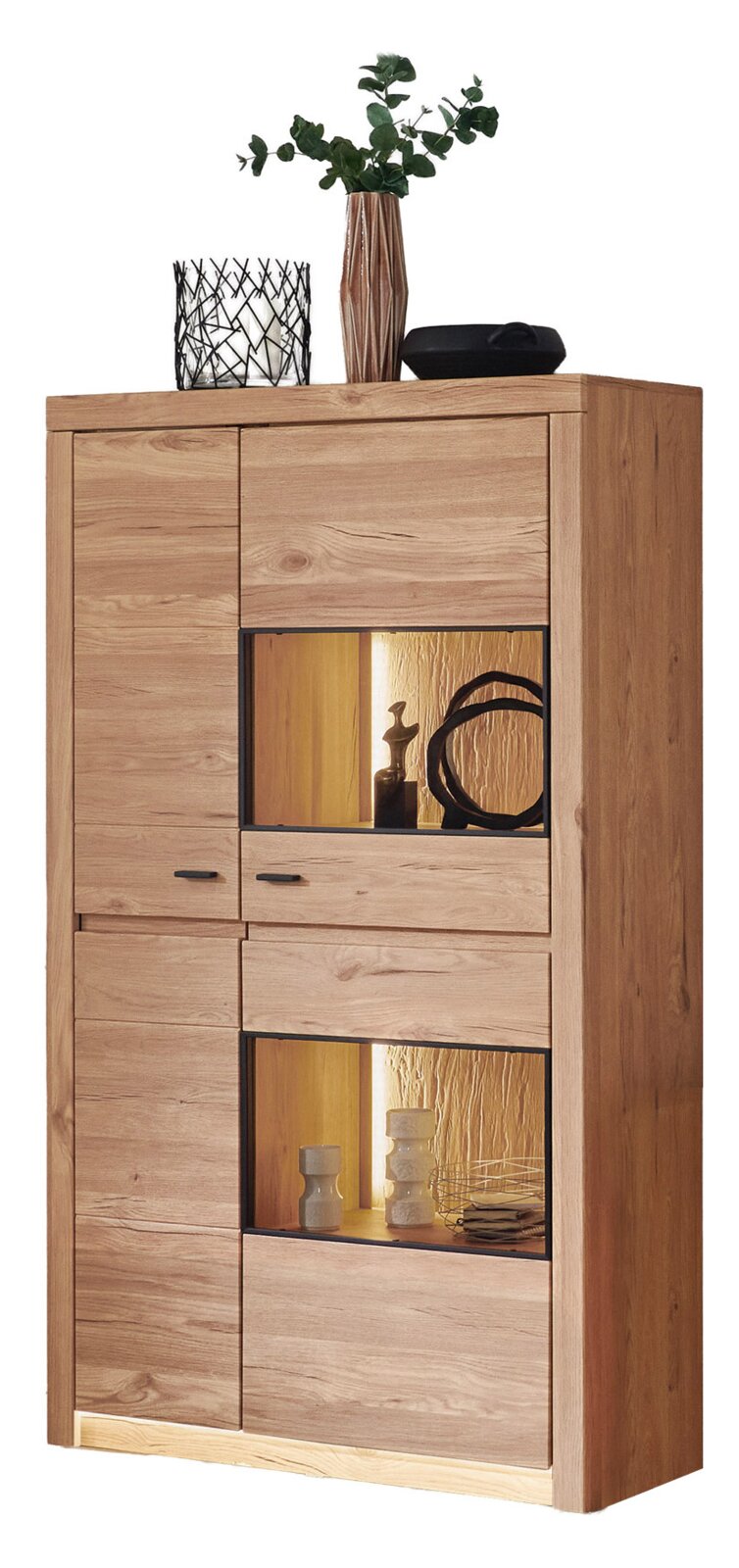 Frontale Ansicht einer hohen, modernen Vitrine/Kommode aus hellem Massivholz mit zwei beleuchteten offenen Fächern und schwarzen Griffen; oben stehen Dekoartikel und eine Vase mit Grünpflanze.