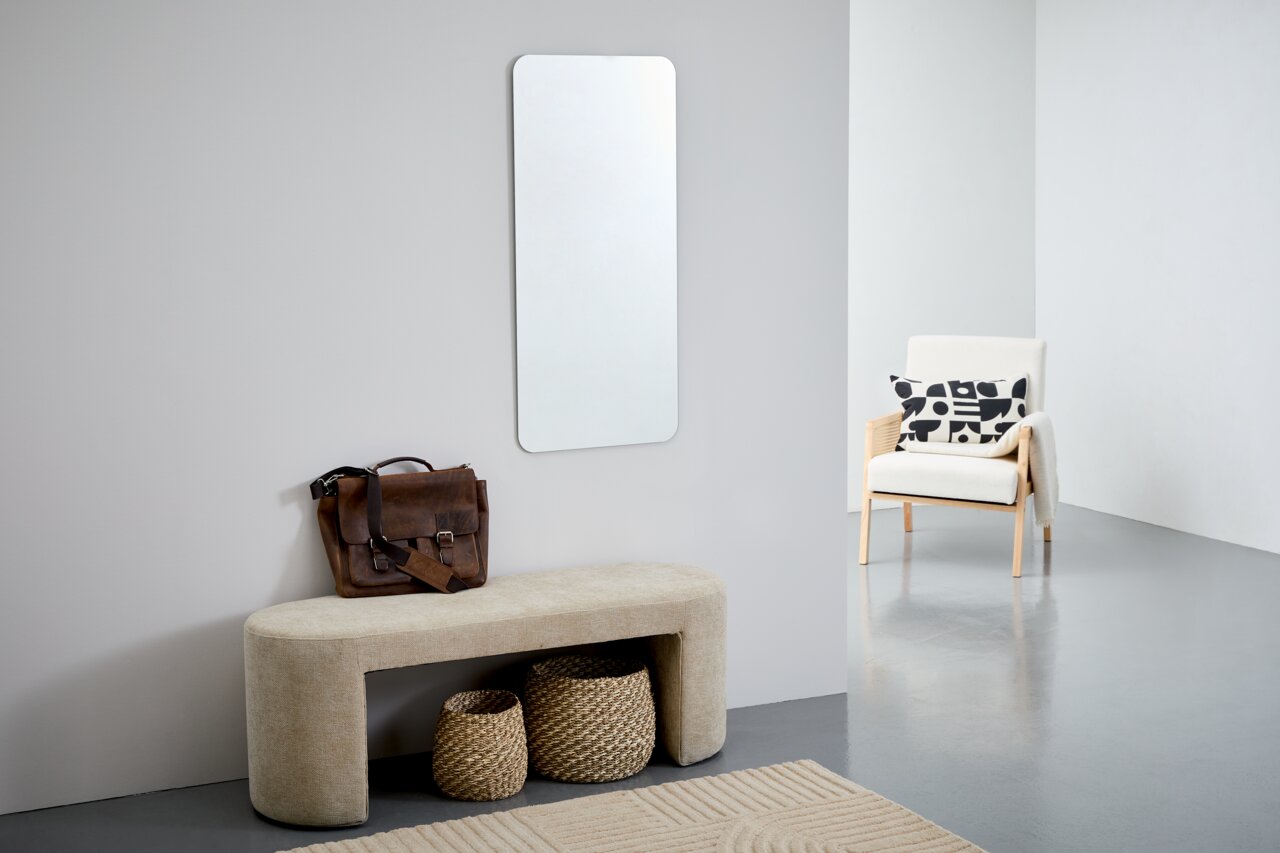 Rechteckiger Wandspiegel ca. 50x110 cm, aufgehängt in einem modernen Raum mit einem beigen Sitzbank, einer braunen Ledertasche und einem weißen Sessel. Perspektive von vorne.