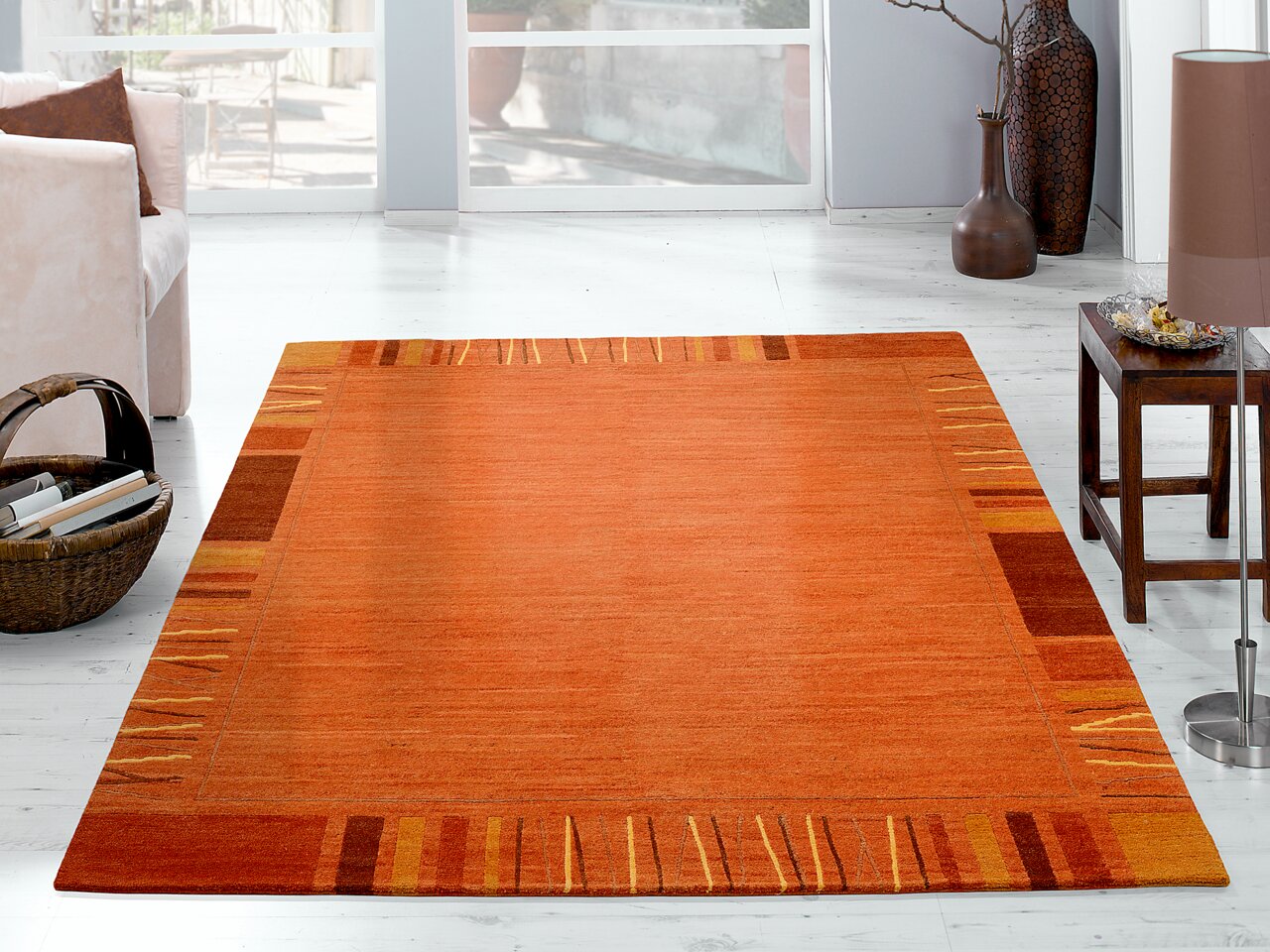 Ein orangefarbener Wollteppich mit geometrischem Muster, in einem hellen Wohnzimmer auf einem weißen Holzboden liegend. Perspektive von schräg oben.