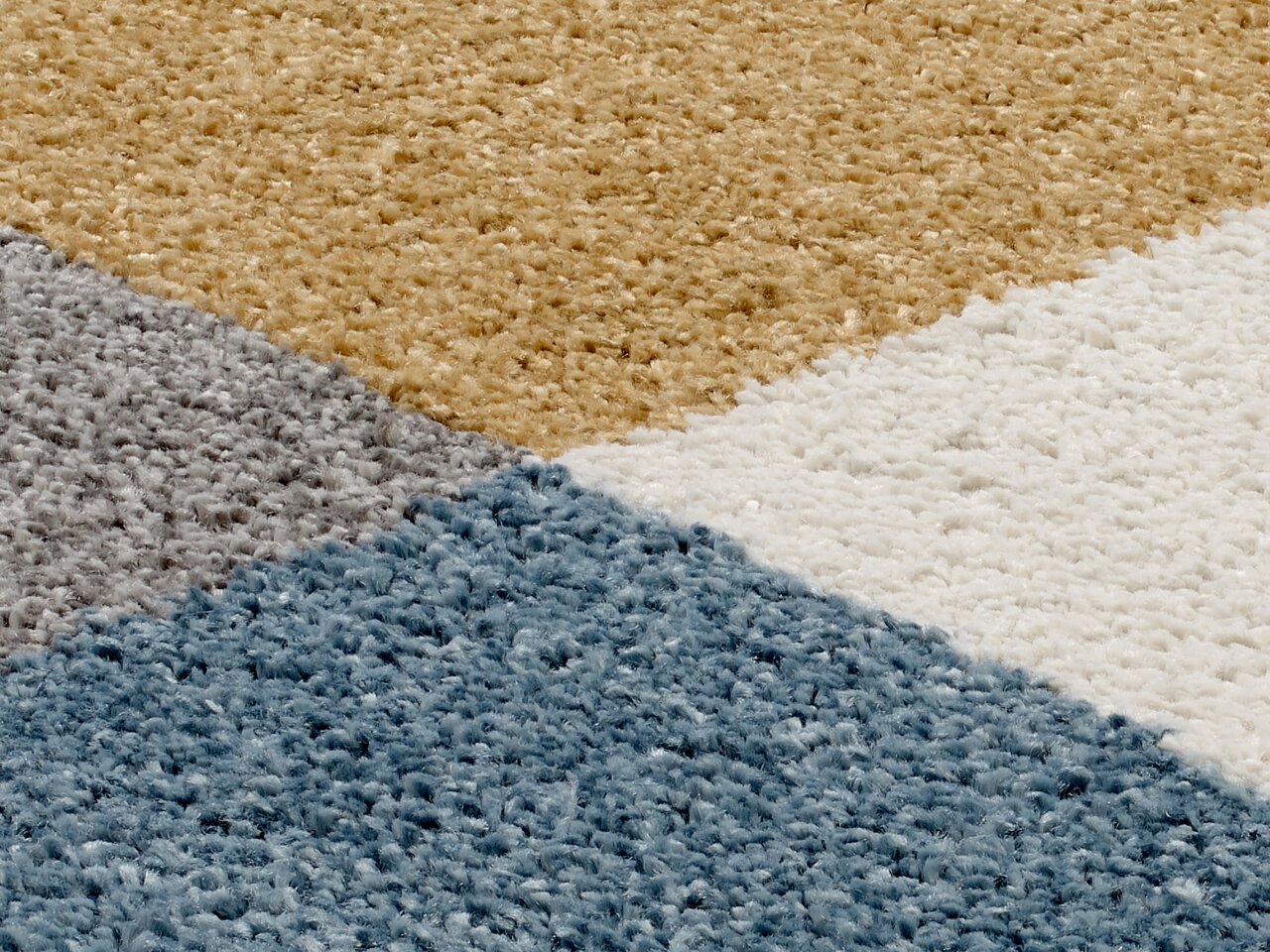 Nahaufnahme eines Uni-Teppichs mit geometrischem Muster in Blau, Grau, Beige und Weiß.