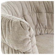 Nahaufnahme eines beigen Armlehnstuhls mit weicher Polsterung und texturierter Oberfläche, seitliche Perspektive.