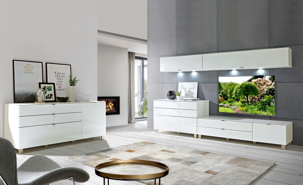 Modernes Wohnzimmer mit weißem TV-Lowboard, Hängeschrank und Sideboard in einer eleganten, hellen Umgebung. Perspektive von vorne.