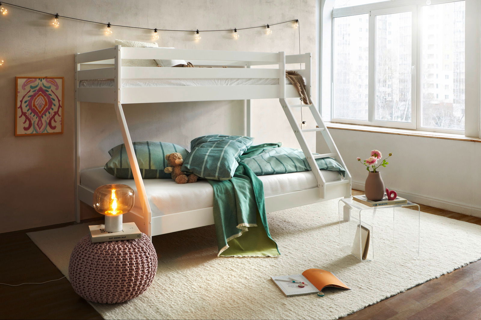 Weißes Etagenbett in einem gemütlichen Schlafzimmer mit Lichterkette, dekorativen Kissen und Decken, aus der Perspektive von vorne rechts.