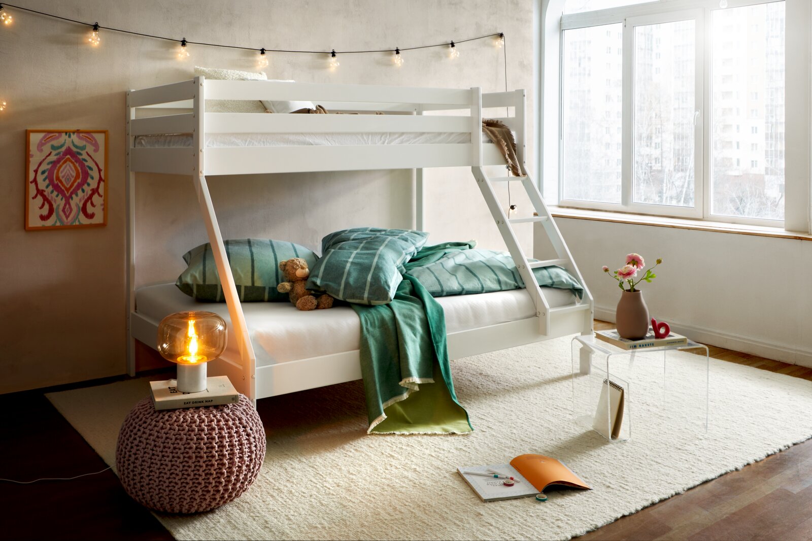 Een wit stapelbed in een gezellige slaapkamer met een lichtslinger, sierkussens en dekens, gezien vanaf de rechterkant van voren.