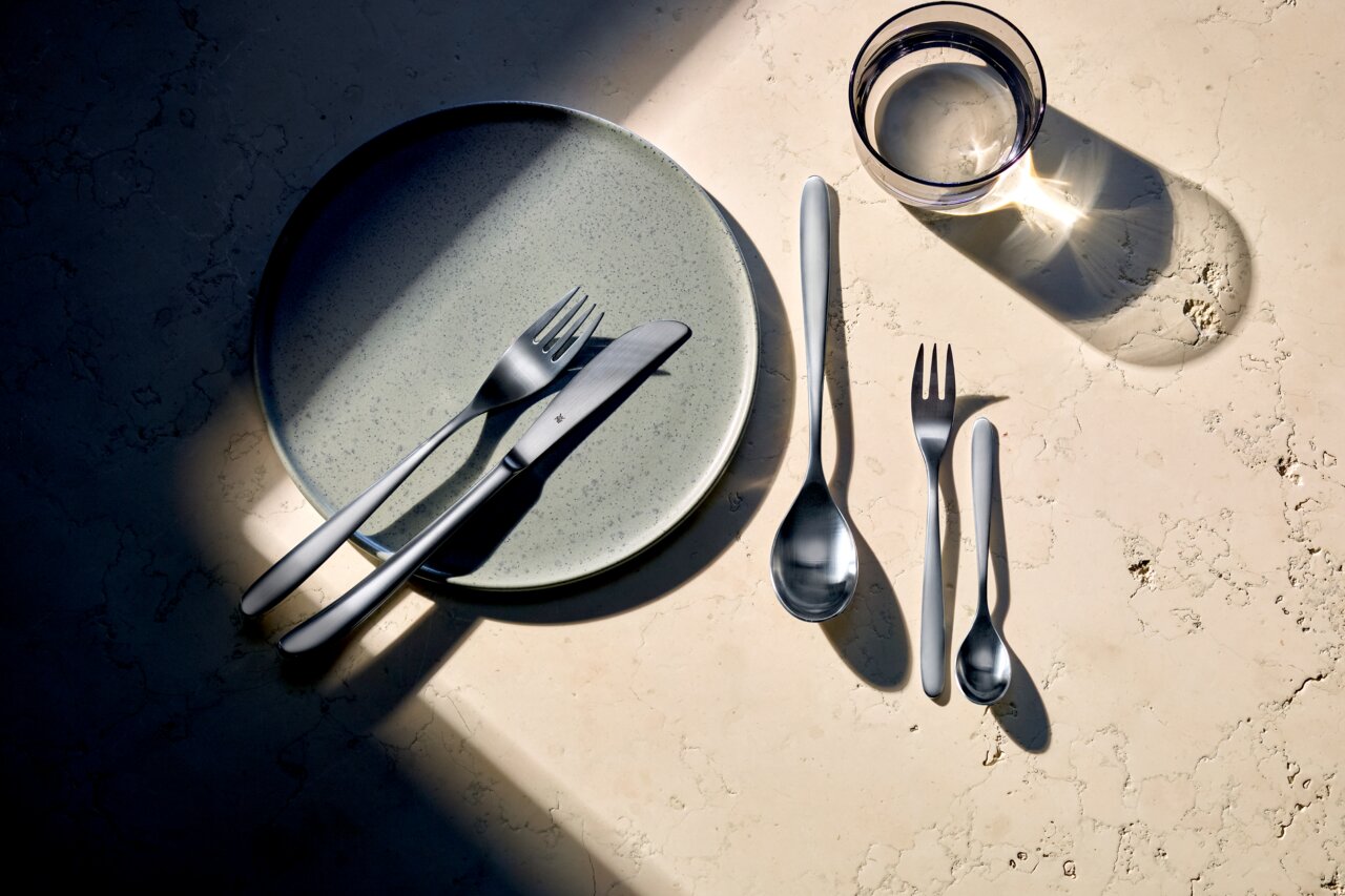 Besteck-Set Silk 60-tlg. auf einem Tisch, bestehend aus Messer, Gabel, Löffel und kleiner Gabel, von oben fotografiert.