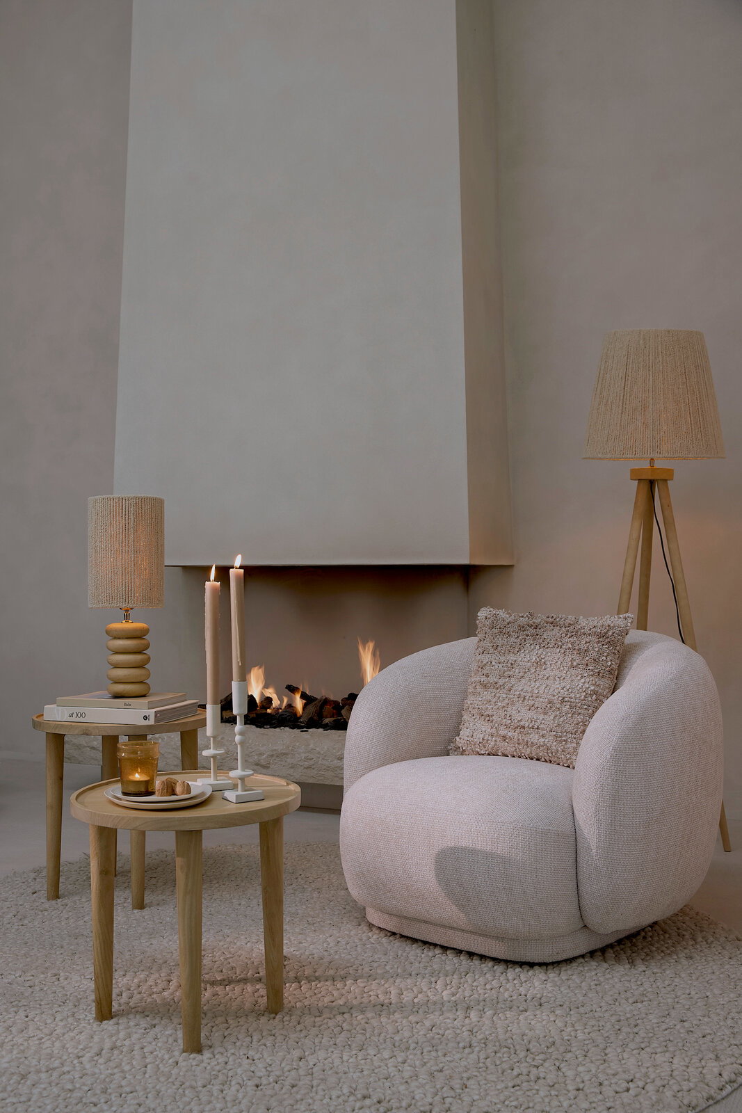 Light&Living Sessel OVITO Gemütlicher, cremefarbener Sessel mit rundem Design, dekoriert mit einem strukturierten Kissen, vor einem modernen Kamin. Perspektive von vorne.