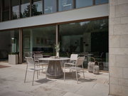 Moderner Stapelsessel auf einer Terrasse, seitliche Perspektive, umgeben von einem eleganten Tisch und dekorativen Laternen.