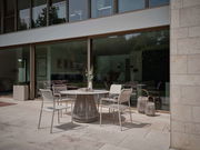 Moderner Stapelsessel auf einer Terrasse, seitliche Perspektive, umgeben von einem eleganten Tisch und dekorativen Laternen.