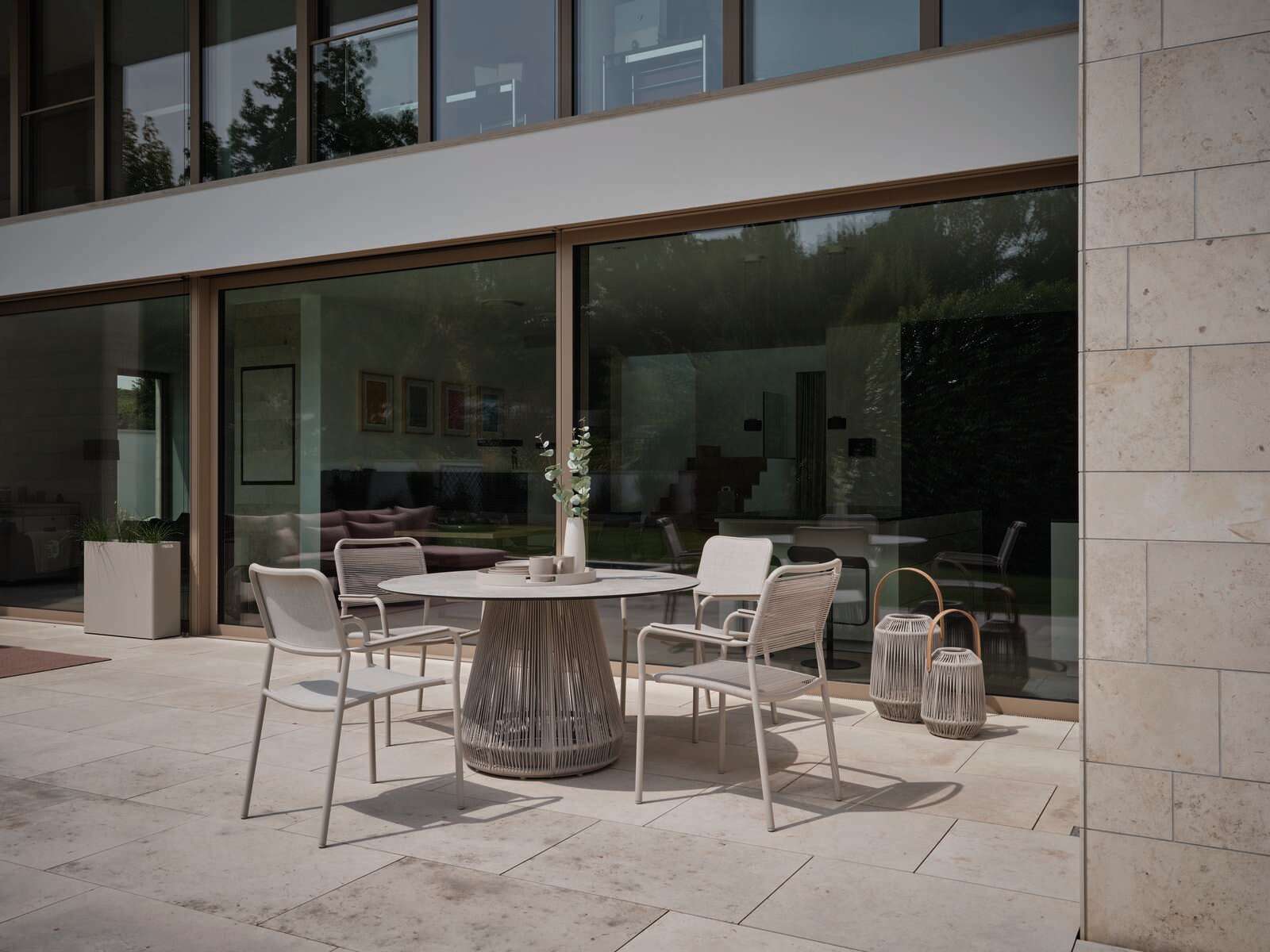 Moderner Stapelsessel auf einer Terrasse, seitliche Perspektive, umgeben von einem eleganten Tisch und dekorativen Laternen.