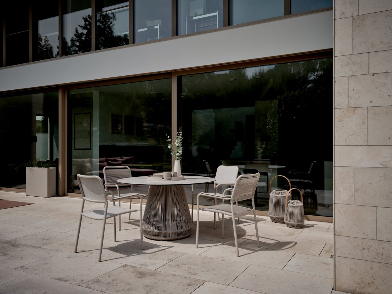 Moderner Stapelsessel auf einer Terrasse, seitliche Perspektive, umgeben von einem eleganten Tisch und dekorativen Laternen.