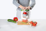 Person benutzt den Nicer Dicer Julietti 13-tlg. aus der Vogelperspektive, um eine Tomate zu schneiden, umgeben von frischem Gemüse auf einem Tisch.