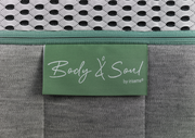 Nahaufnahme einer Matratze mit grünem Etikett 'Body & Soul by irisette', grauer Stoff und weißem Netzgewebe.
