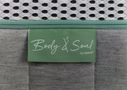 Nahaufnahme einer Matratze mit grünem Etikett 'Body & Soul by irisette', grauer Stoff und weißem Netzgewebe.