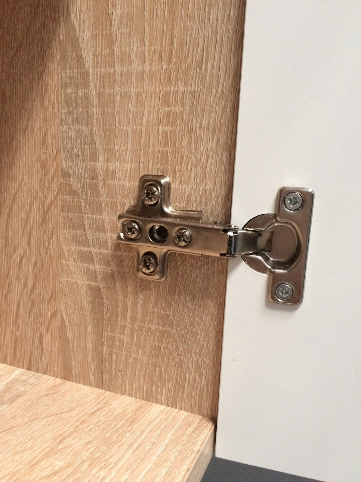 Nahaufnahme einer Metallscharnierbefestigung an einem Küchenschrank, Perspektive von vorne.