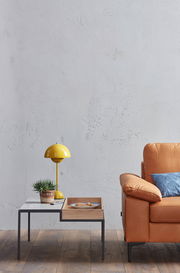 Seitliche Ansicht eines modernen 2,5-Sitzer Sofas in hellbraunem Leder, neben einem Couchtisch mit gelber Lampe und Pflanze.