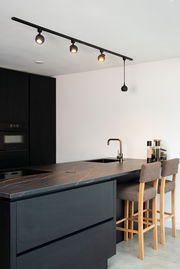 Moderne schwarze Strahler auf einer Schiene in einer stilvollen Küche, seitliche Perspektive.