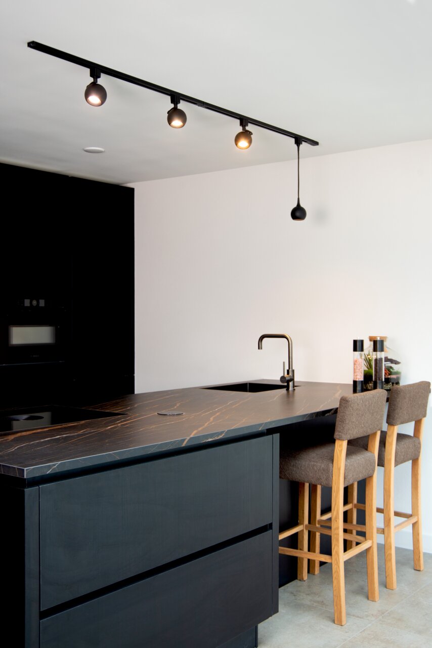 Moderne schwarze Strahler auf einer Schiene in einer stilvollen Küche, seitliche Perspektive.