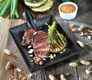 Schwarzer Steak-Servierteller mit gegrilltem Steak, Spargel und Ananas, dekoriert mit Nüssen, aus der Vogelperspektive.