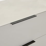 Detailaufnahme einer weißen, glatten Schrank- oder Kommodenfront mit zwei langen, mattschwarzen Griffleisten, fotografiert in schräger Perspektive von oben