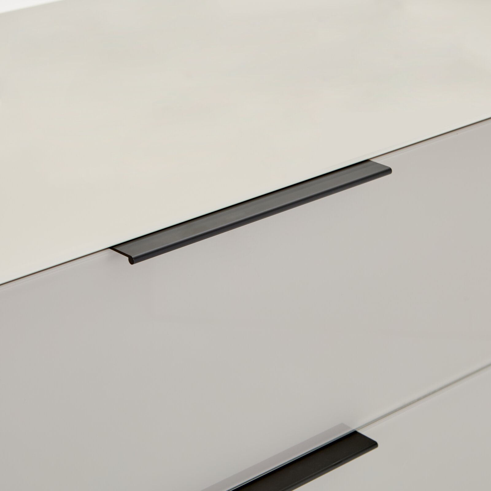 Detailaufnahme einer weißen, glatten Schrank- oder Kommodenfront mit zwei langen, mattschwarzen Griffleisten, fotografiert in schräger Perspektive von oben