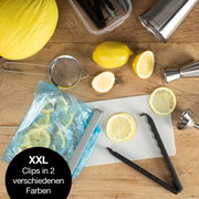 Verschlussclips XXL in zwei Farben, von oben fotografiert, umgeben von Küchenutensilien und Zitronen.