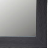 Nahaufnahme eines rechteckigen Spiegels mit dunklem, strukturiertem Rahmen, perspektivisch von der Ecke aus gesehen.