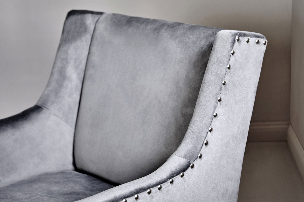 Grauer Samtstuhl mit Nietenverzierung, Nahaufnahme der Rückenlehne und Armlehne von der Seite.
