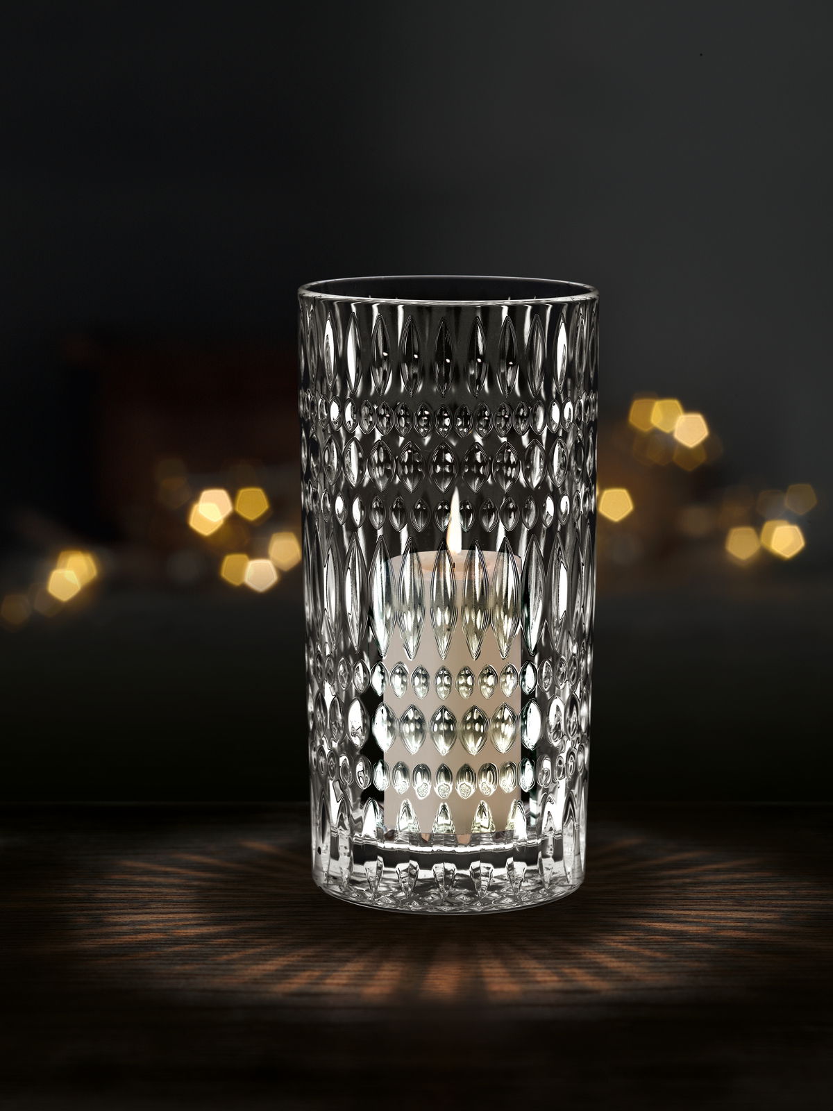 Kristallklare Vase oder Windlicht mit strukturiertem Muster, beleuchtet von einer Kerze, auf dunklem Hintergrund, frontal betrachtet.