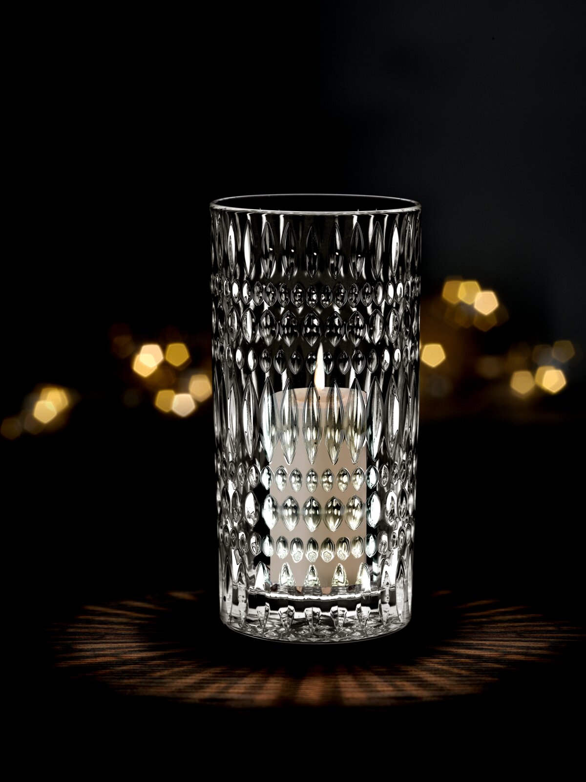 Kristallklare Vase oder Windlicht mit strukturiertem Muster, beleuchtet von einer Kerze, auf dunklem Hintergrund, frontal betrachtet.
