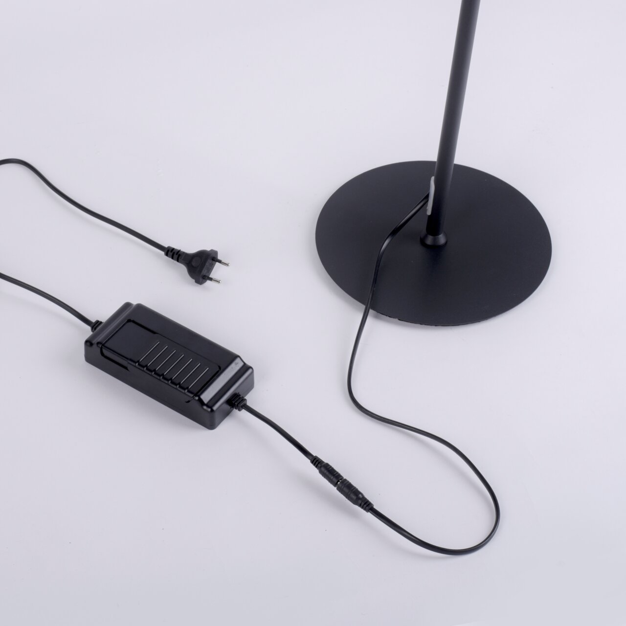 Nahaufnahme der Basis einer schwarzen Stehleuchte CURLS mit Stromkabel und Stecker.