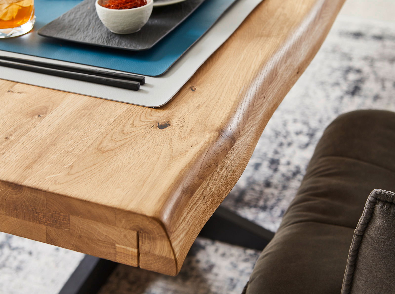 Nahaufnahme eines Esstisches aus Holz mit natürlicher Kante, darauf Tischsets und Geschirr, seitliche Perspektive.